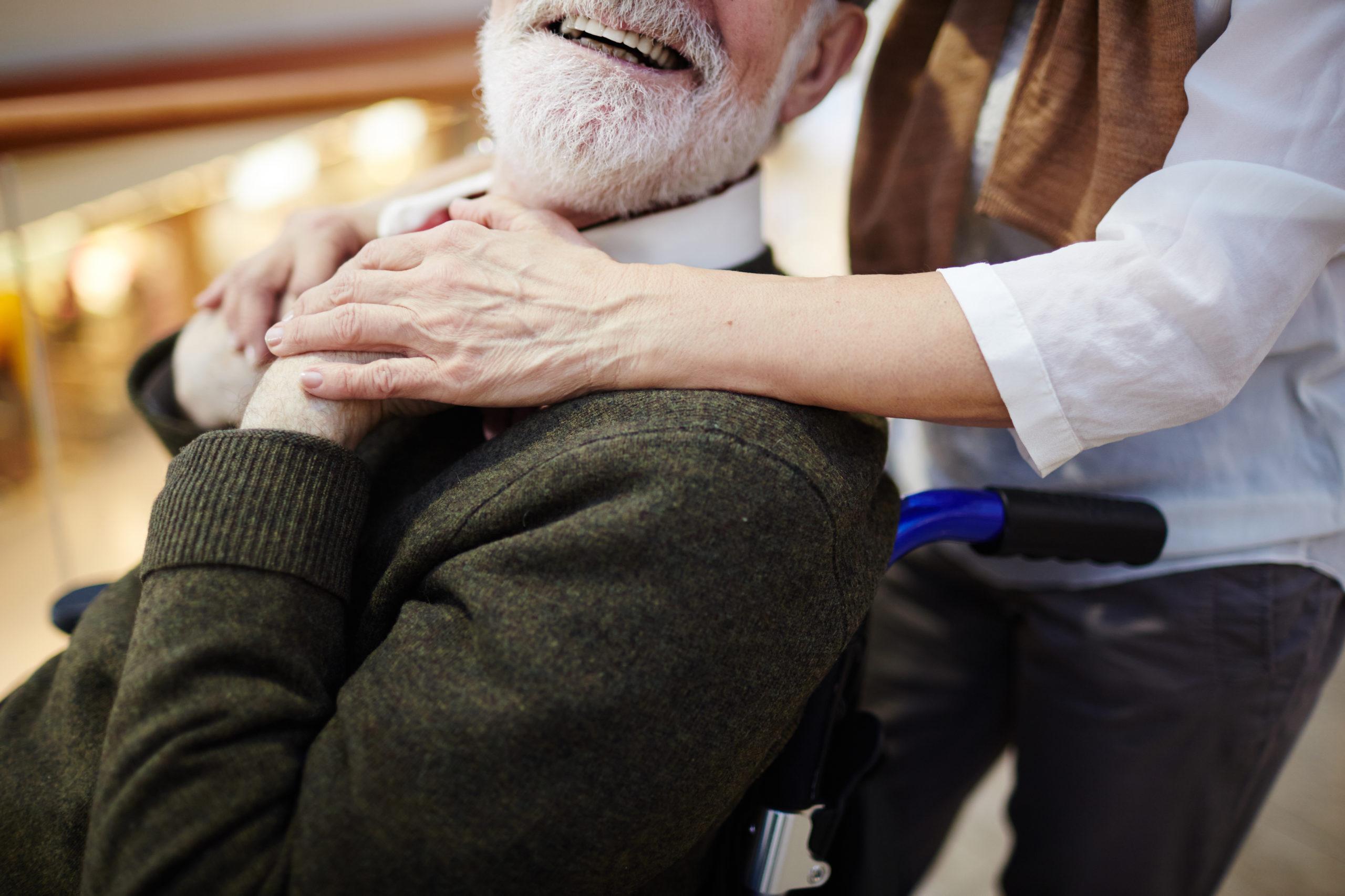 Smiling aged man in wheelchair and his caregiver